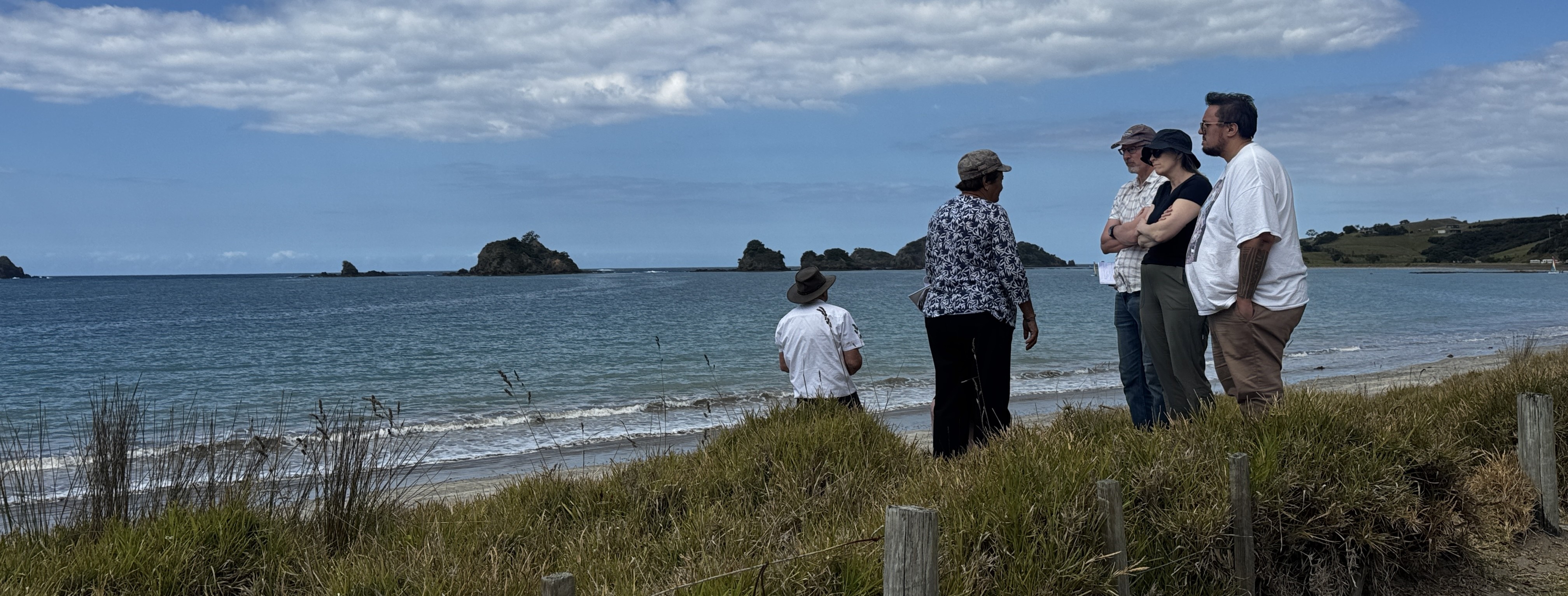 People talking and listening intently, standing in the dunes of a Northland beach.